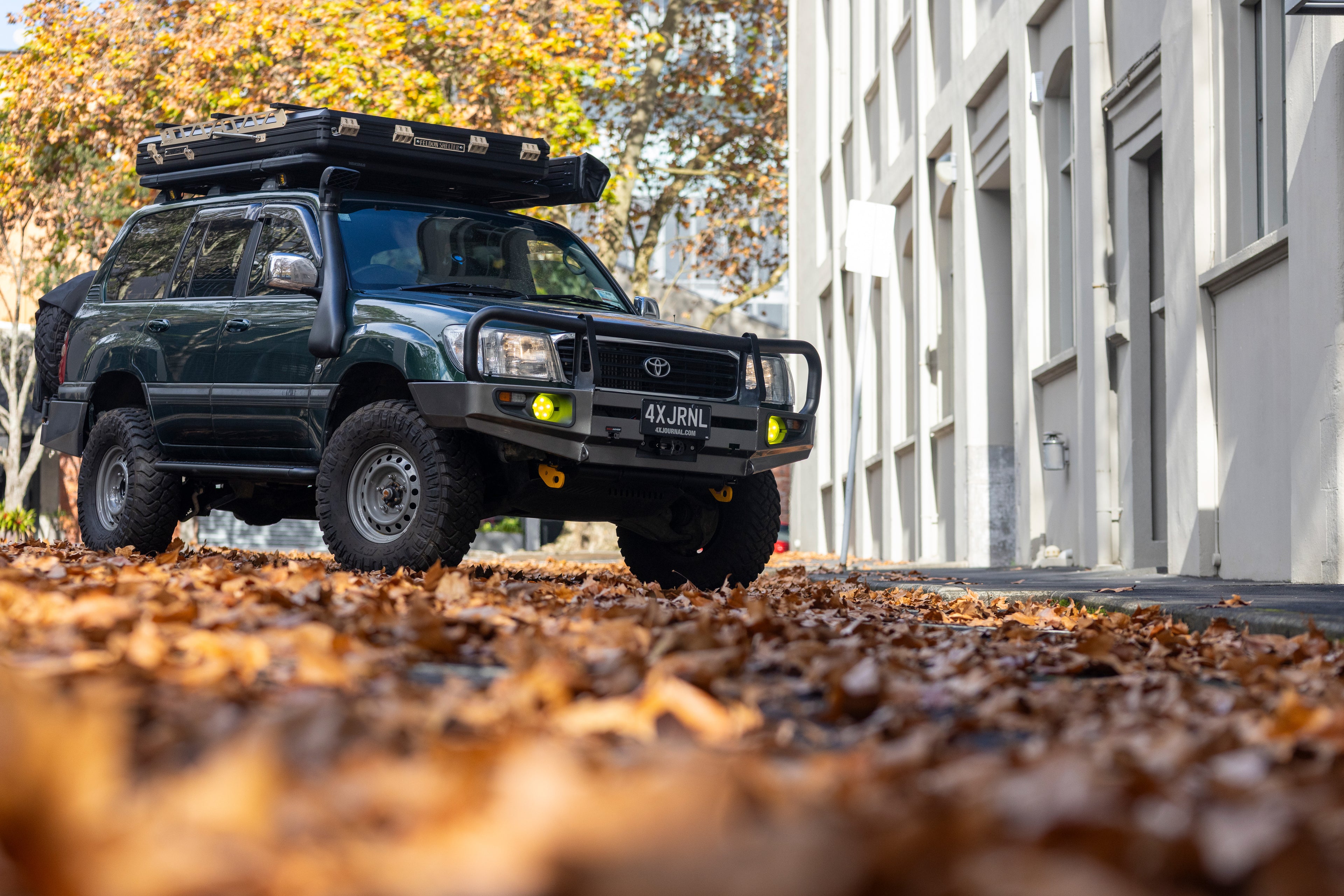 Black Toyota truck with roof rack on a street with fallen leaves
